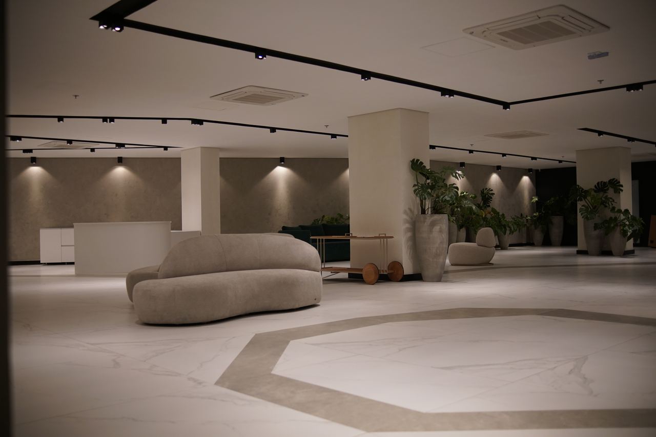 Lobby amplo com piso de mármore, sofá curvo, iluminação em trilhos e plantas