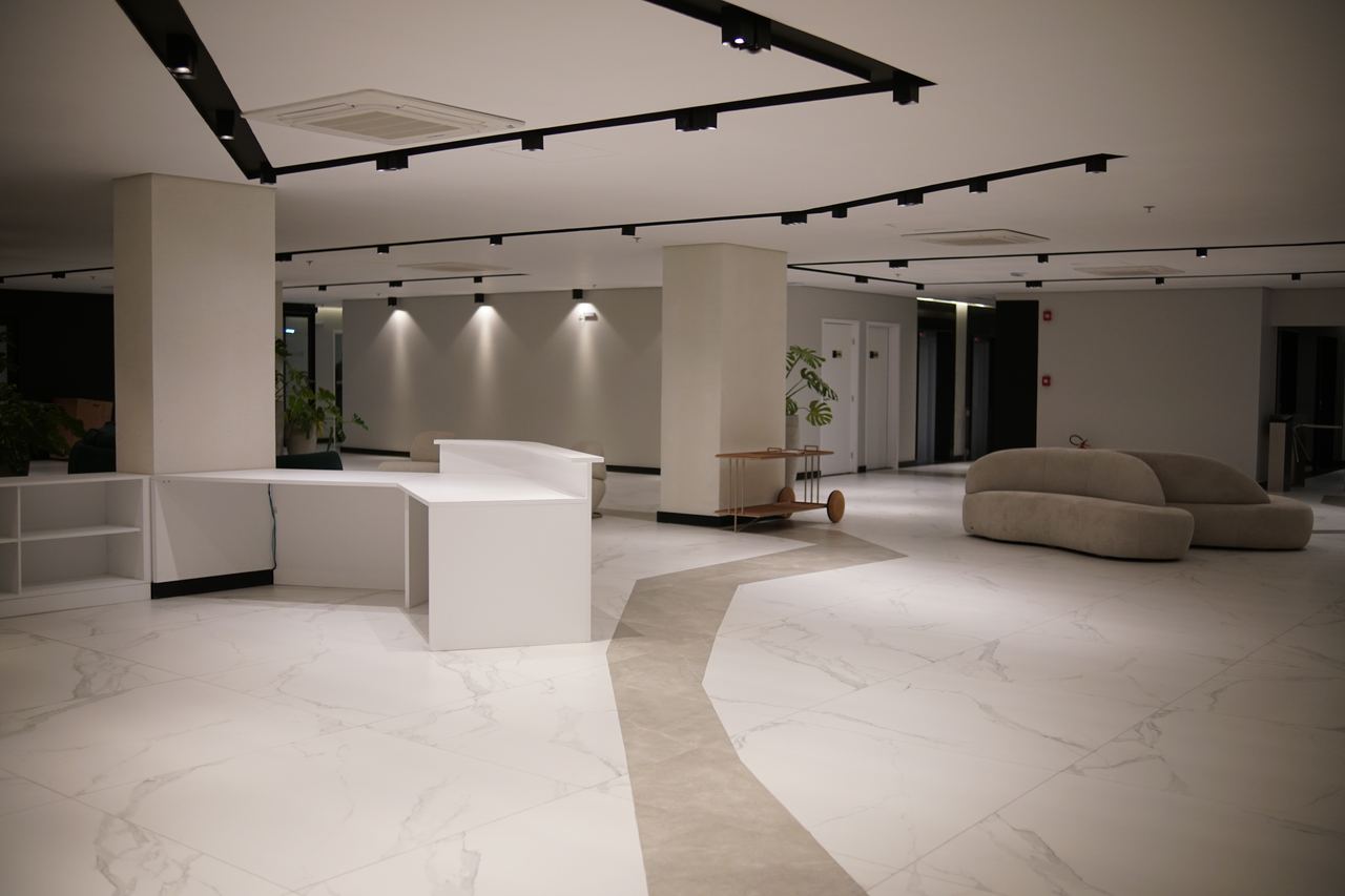 Hall de atendimento com balcão branco, sofás curvos e acesso aos elevadores